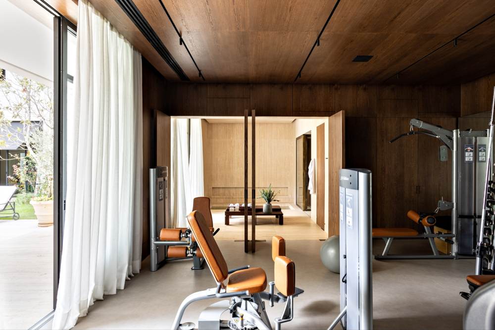 Ambiente com forro de madeira, cortinas claras e equipamentos de academia