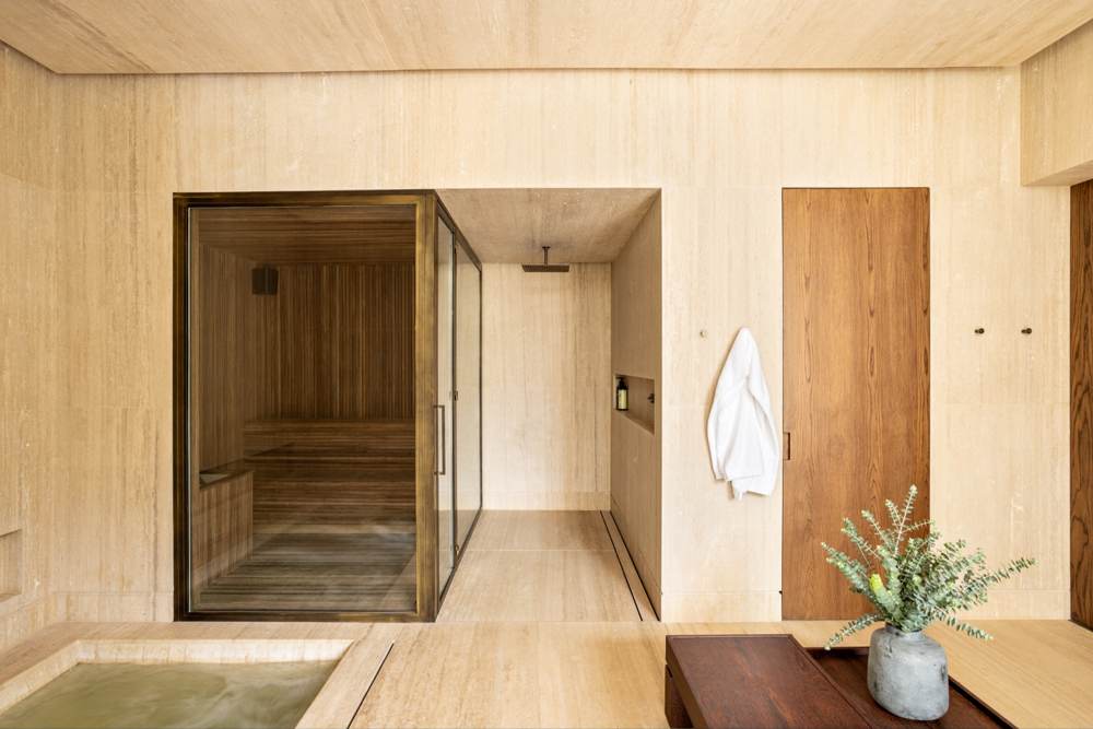 Sauna com revestimento em madeira clara e porta de vidro