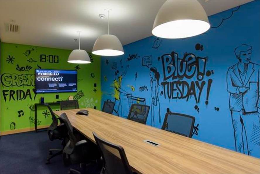 Sala de reunião com mesa longa de madeira e parede ilustrada em azul