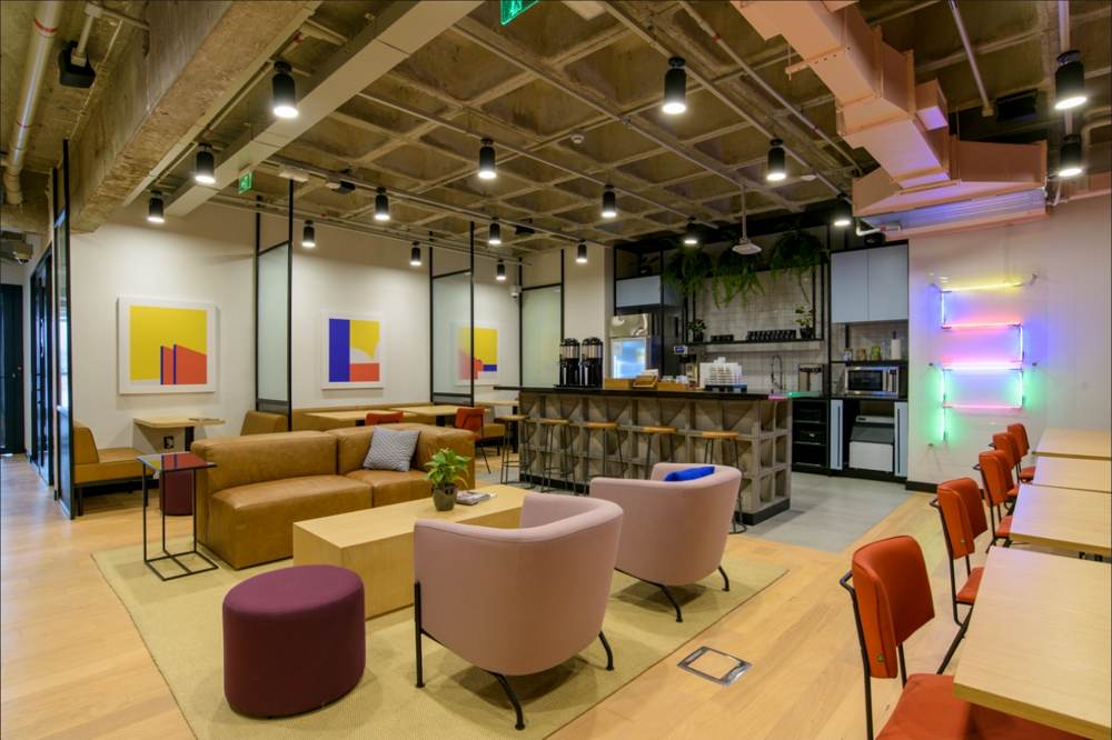Espaço de convivência com poltronas coloridas, estante e iluminação aparente